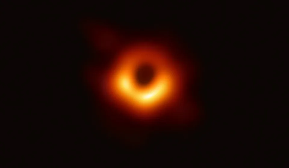 An uneven bright radio ring surrounds a dark centre, with the lower arc brighter than the upper arc.