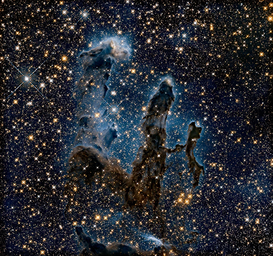 The pillars become faint silhouettes among many stars in this infrared view, though dense dusty regions still obscure light.