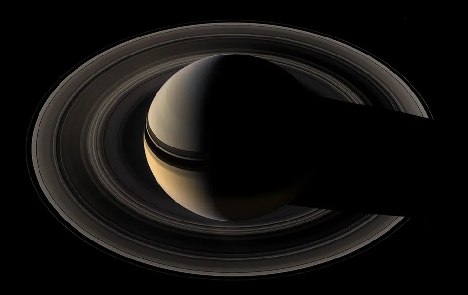 Broad thin rings surround Saturn and cast dark bands across the planet's cloud tops.